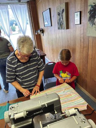 HEMMING Debbie Sneed assists Zoee Ray with the hem of her apron during the 4-H sewing class last Wednesday. | XANE REITER PHOTO