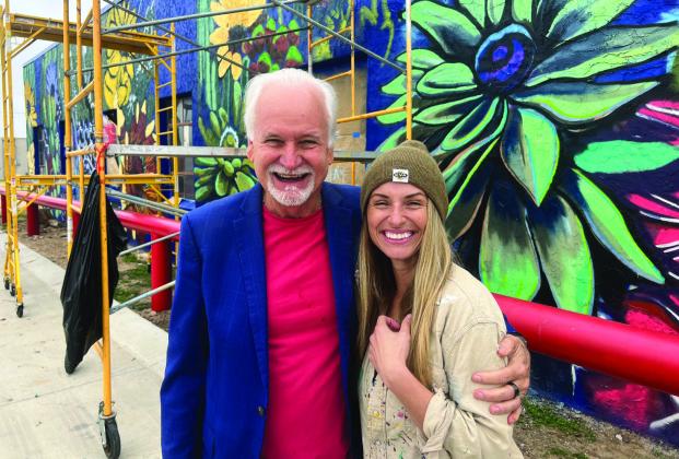 “Cal”and Kurt Kizer take time for photos in front of the street art Cal is painting on the WIC Building. She started the work a few weeks ago and hopes to be completed by mid-December. This is one of the four murals she is contracted to paint.