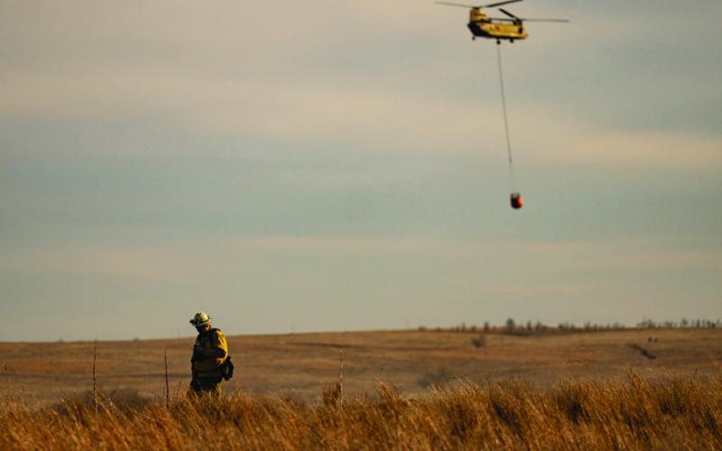 FIREAFTERMATH AfirefighterwalksaridgelineasaChinookhelicopter fliesoverranchlandcarryingwatertodumpontheSmokehouseCreek Fire in the Texas Panhandle after high winds reignited the record breaking fire. |TEXAS A&amp;amp;M AGRILIFE SAM CRAFT PHOTO