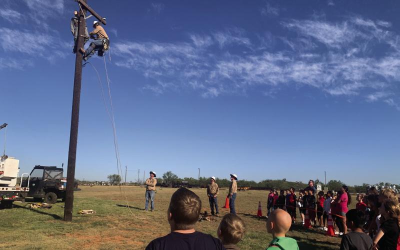 SURVIVAL PRACTICE Over 300 students from surrounding schools participated in South Plains Electric Company (SPEC) field trip. Students learned the importance of safety when working with electricity. New recruit Woodrow climbed the pole to save the dummy, Bob. The young onlookers watch with anticipation at what will happen next. | ANNA GIBSON PHOTO