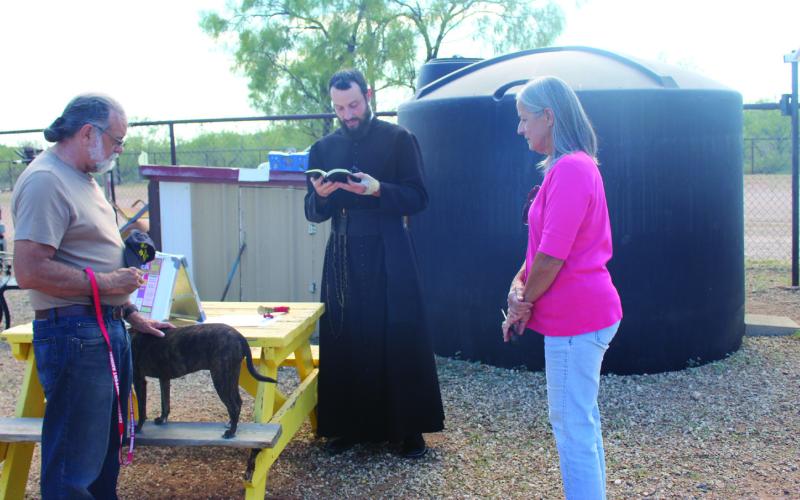 Father Jacob Powell of Holy Cross Catholic Church offered the Blessing of the Animals at the Post Animal Refuge Center last Tuesday during the feast of St. Francis of Assisi. Rick Jones, a volunteer at PARC, is shown with his dog as Father Powell gave the blessing, and Janice Plummer, also a PARC volunteer watches. Photo Provided