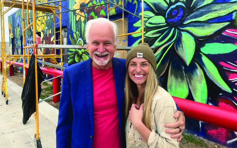 “Cal”and Kurt Kizer take time for photos in front of the street art Cal is painting on the WIC Building. She started the work a few weeks ago and hopes to be completed by mid-December. This is one of the four murals she is contracted to paint.