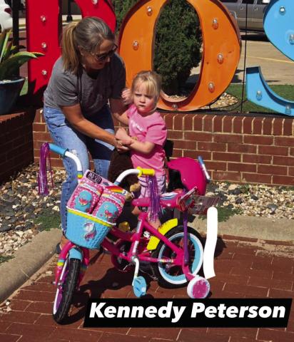 DRAWING WINNER Kennedy Peterson is presented with a 12”girls’ bike, knee and elbow pads, and helmet by Chris Atkinson from the Post Community Recovery Center after the bike drawing on July 4. | DAWN GRAVES PHOTO