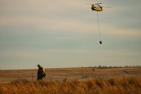 FIREAFTERMATH AfirefighterwalksaridgelineasaChinookhelicopter fliesoverranchlandcarryingwatertodumpontheSmokehouseCreek Fire in the Texas Panhandle after high winds reignited the record breaking fire. |TEXAS A&amp;M AGRILIFE SAM CRAFT PHOTO