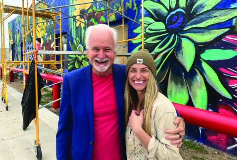 “Cal”and Kurt Kizer take time for photos in front of the street art Cal is painting on the WIC Building. She started the work a few weeks ago and hopes to be completed by mid-December. This is one of the four murals she is contracted to paint.