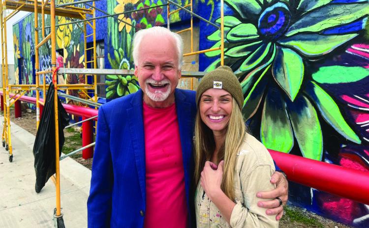 “Cal”and Kurt Kizer take time for photos in front of the street art Cal is painting on the WIC Building. She started the work a few weeks ago and hopes to be completed by mid-December. This is one of the four murals she is contracted to paint.